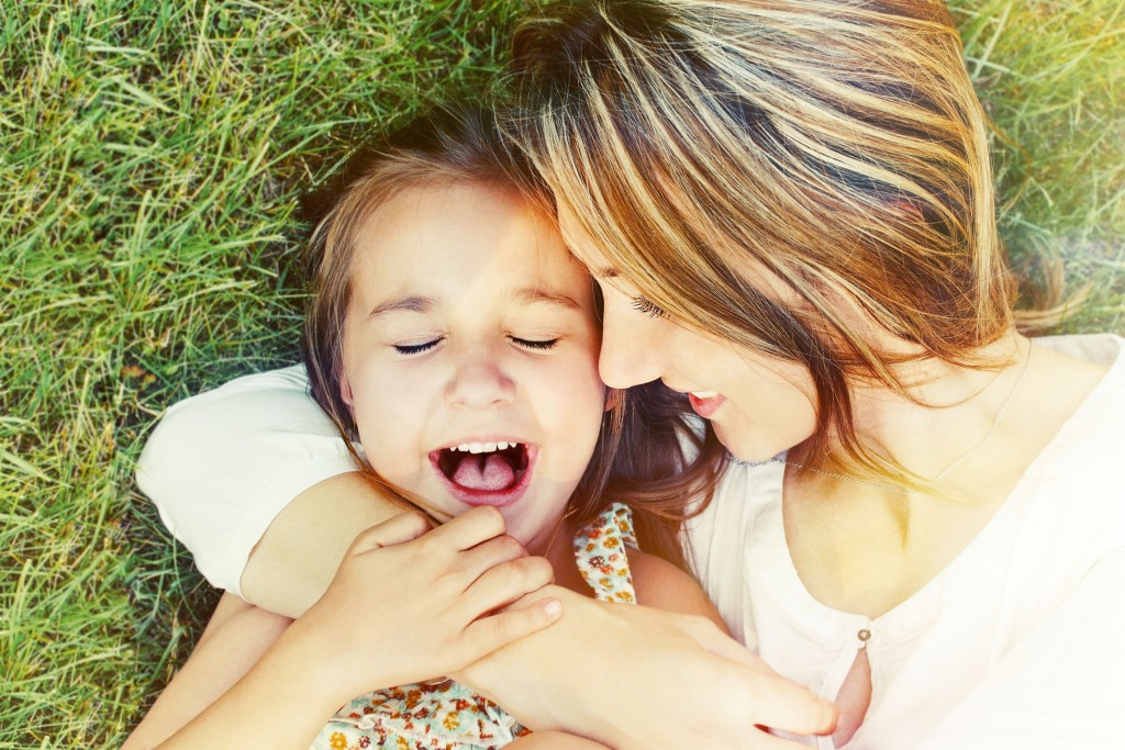 happy little girl and her mother having fun outdoors on the green grass in sunny summer day